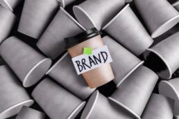 one coffee cup in color with a brand label on it over a pile of plain ones